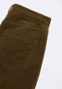 Ruskeat housut, joissa on teksturoitu kangas, takatasku, vyölenkit ja suora leikkaus. Materiaali näyttää tukevalta ja kestävältä.