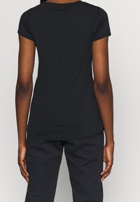 Svart T-shirt med korta ärmar i texturerat tyg, med en enkel design och en mittsöm längs ryggen.