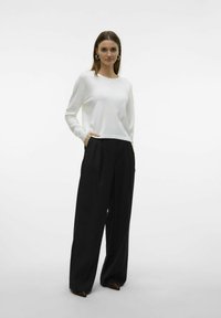 Top bianco a maniche lunghe con scollo rotondo, abbinato a pantaloni neri a gamba larga. Tessuto liscio, con tasche laterali visibili e pieghe.
