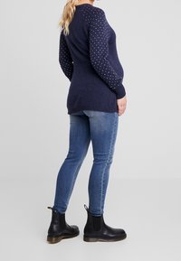 Pull marine avec manches texturées à pois ; associé à un jean skinny bleu et des bottines noires. Matière en tricot, col rond, coupe décontractée.