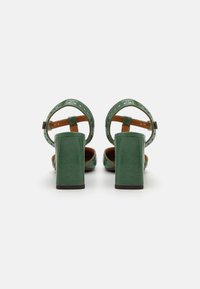 Green leather platform heels with a thick block heel, open toe, and ankle strap featuring perforated accents. Brown insoles visible.