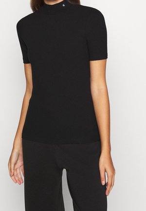 Black ribbed short-sleeve top with a high neckline, featuring a small logo accent near the collar. Soft texture and fitted design.