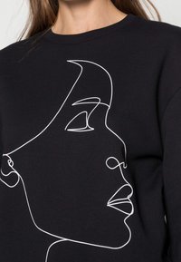 Sudadera negra con un contorno blanco de una cara, que muestra líneas suaves y un diseño minimalista que resalta sobre la tela.