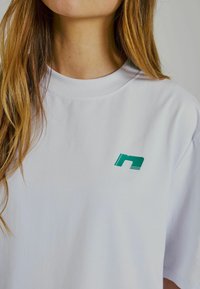 Vit bomull t-shirt med rund halsringning, lös passform och en liten grön grafisk design på vänster bröstområde.