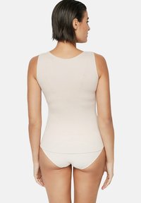 Débardeur ajusté beige clair en tissu doux et extensible, avec un col arrondi et sans motifs ni éléments en métal visibles.