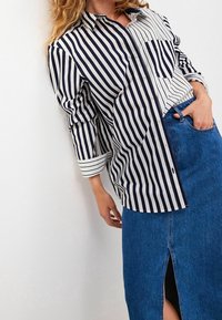 Striped button-up shirt in navy and white, featuring a single chest pocket and rolled sleeves, paired with a knee-length denim skirt with a slit.