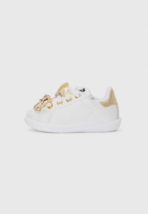 Hvit sneaker med gulldetaljer, med en fluffy krage og dekorative aksenter på snøringen. Glatt materiale og flat hvit såle.