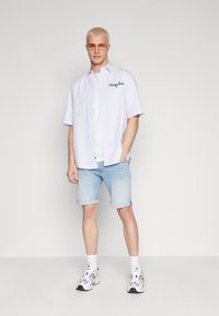 Camisa de manga corta blanca con rayas azul claro y logo bordado, combinada con pantalones cortos de mezclilla azul claro y zapatillas blancas.