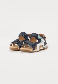 Blue and white leather sandals with open toe, adjustable straps, and a textured brown sole featuring a wavy pattern.