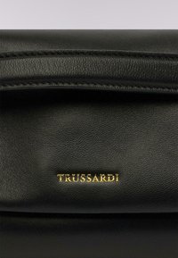 Černá kožená kabelka s hladkým povrchem, s pozlaceným logem "TRUSSARDI" a jemnými švy podél okrajů.