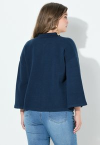 Navyblaues, oversized Sweatshirt mit weiten Ärmeln, strukturiertem Strick und hohem Kragen, kombiniert mit hellblauen, taillierten Jeans.
