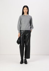 Grauer gestrickter Pullover mit kurzen Ballonärmeln und drei Knöpfen an der Schulter, kombiniert mit schwarzen Leder-Hose im Weitschnitt und Plateauschuhen.