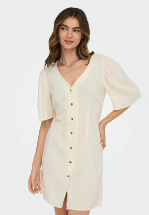 Robe courte beige avec un décolleté en V, des manches évasées et un devant à boutons avec des boutons de couleur dorée. Fabriquée en tissu léger.