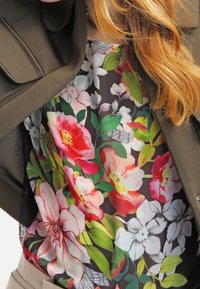 Blomstret bluse med livlige farver, der har rosa, hvide og grønne blomster på en mørk baggrund og et løst, svævende design.