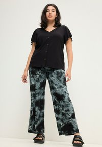 Černý žebrovaný top s výstřihem do V a krátkými volánovými rukávy, doplněný o knoflíky. K tomu široké kalhoty s modro-černým tie-dye vzorem. Černé platformové sandály.