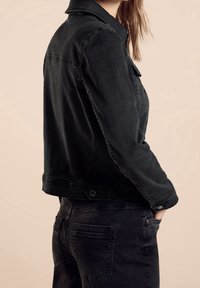 Svart denimjacka med klassisk krage, sidfickor och knäppning i ärmsluten. Texturerad tyg med en lätt blekt finish.