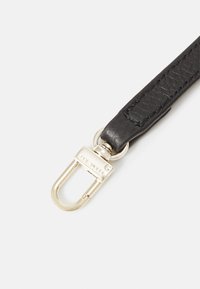 Sangle en cuir noire avec mousqueton en métal argenté attaché, montrant une texture et des coutures en gros plan sur un fond clair uni.