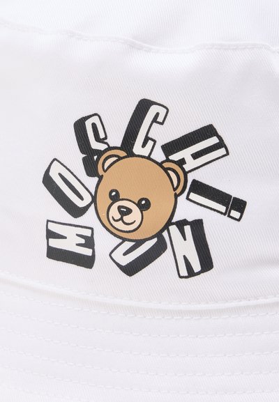 Πρόσωπο αρκούδας Teddy περιβαλλόμενο από στυλιζαρισμένα ανακατεμένα μαύρα και λευκά γράμματα σε λευκό ύφασμα.