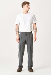 Grå skræddersyede bukser med en glat overflade, plisseret foran og sidelommer, parret med en ensfarvet hvid t-shirt og brune sko.