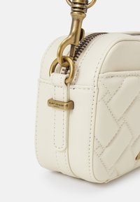 Borsa a tracolla bianca in pelle con motivo trapuntato, hardware dorato e chiusura con zip. Include un dettaglio con etichetta di marca.