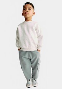 Felpa grigio chiaro con motivo maculato, abbinata a pantaloni cargo larghi azzurri chiari. Il bambino indossa scarpe da ginnastica bianche e grigie.