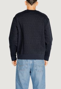 Felpa navy con un delicato motivo a logo, colletto rotondo, polsini e orlo a coste, abbinata a jeans azzurri chiari. Tessuto strutturato.