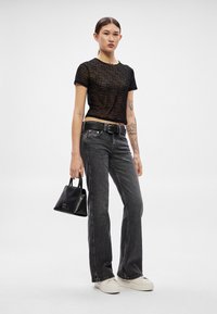 Čierne krátke sieťované tričko s potlačou textu, skombinované s tmavosivými džínsami s vysokým pásom, čiernym opaskom, malou čiernou kabelkou a bielymi teniskami.