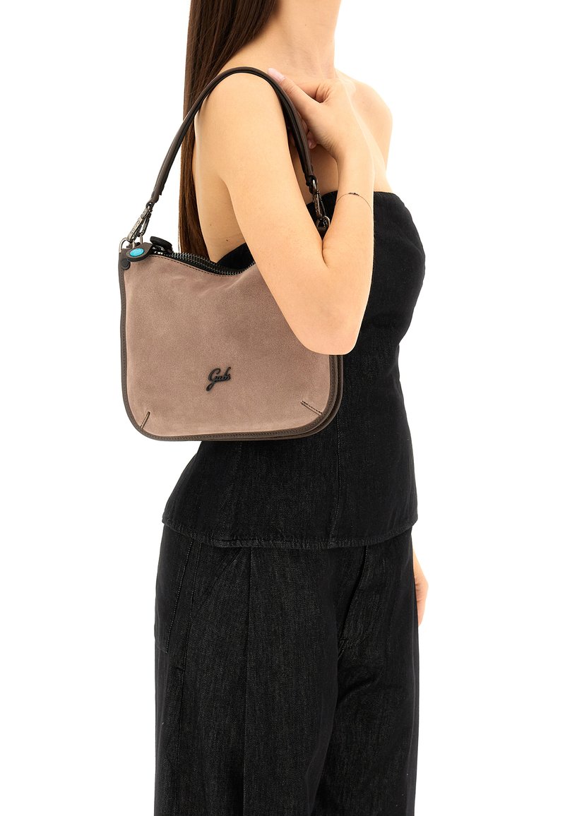 Bolso de hombro de ante marrón con detalles negros, que cuenta con un cierre de cremallera y un acento cerca de la cremallera. Forma compacta y rectangular.