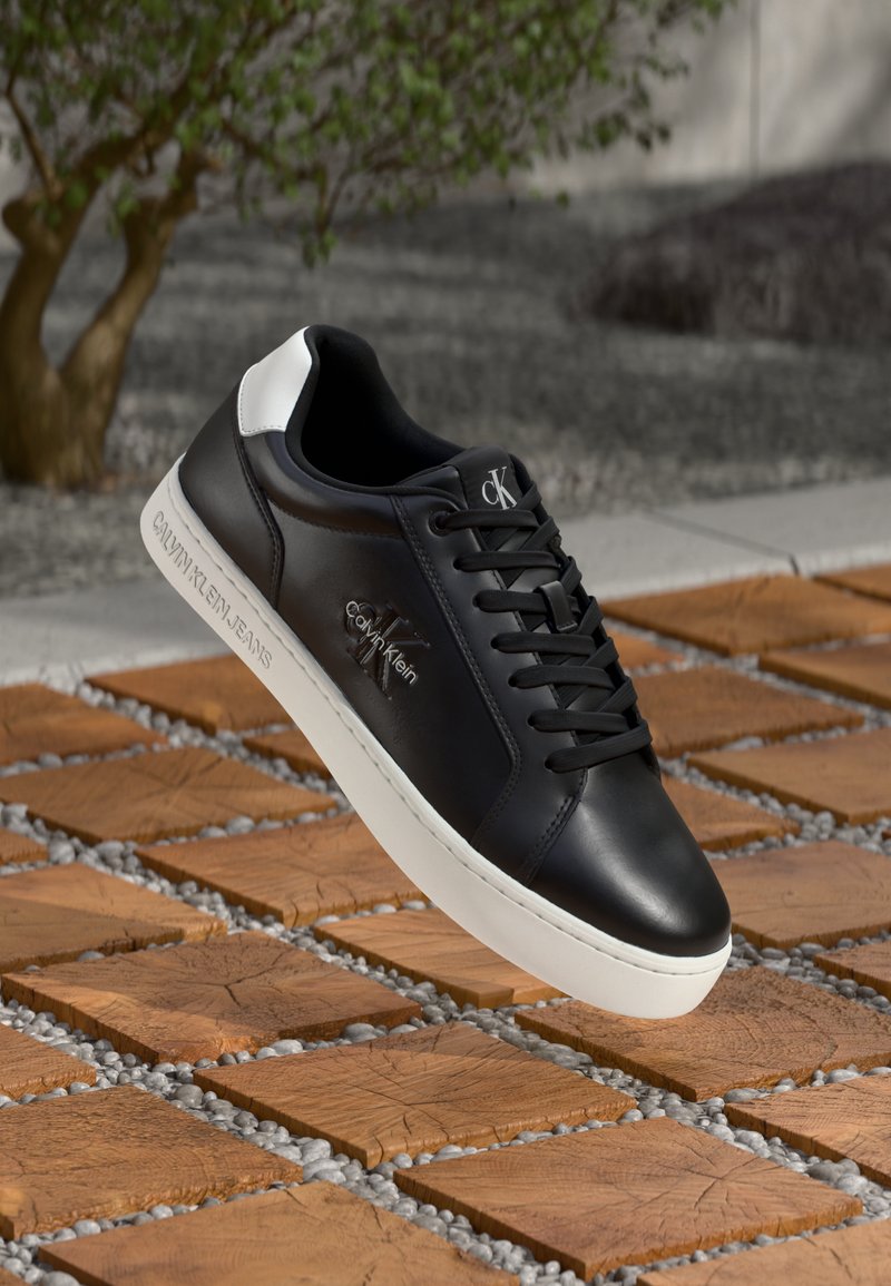 Zwarte leren sneaker met witte accenten, ronde neus en zwarte veters. Heeft een logo aan de zijkant en subtiele branding op de zool.
