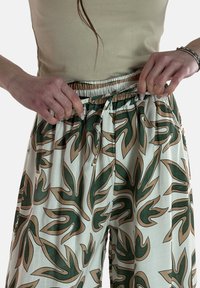 Crème broek met een groen en beige bladerenpatroon, elastische tailleband en trekkoord. Gemaakt van lichtgewicht stof met een gladde textuur.