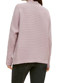  Lichtroze geribde trui met een hoge hals, voorzien van horizontale lijnen en een zachte, losse pasvorm. De textuur lijkt zacht en gebreid te zijn.