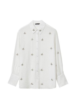 Camicia bianca con bottoni, realizzata in un tessuto texturizzato, con ricami a forma di ape argentata nella parte anteriore e maniche lunghe leggermente gonfiate.