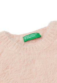 Collo di un morbido pullover di un rosa pallido con un'etichetta di stoffa verde che legge "United Colors of Benetton" cucita all'interno del colletto.