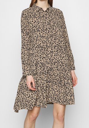 Leopardenmuster-Kleid aus beigem Stoff mit Knopfleiste, langen Ärmeln und gestuftem Rüschensaum. Schwarze Flecken über das gesamte Kleid verteilt.