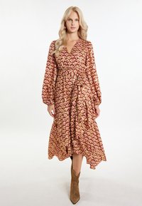 Rochie cu model roșu și auriu, cu mâneci lungi, stil înfășurat și tiv ondulat. Modelul poartă cizme până la gleznă de culoare maro, cu o croială lejeră.