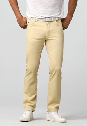 Light beige chinos with a straight leg design, made from cotton, featuring front pockets and a lightweight woven belt. Worn with white sneakers.