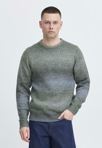 Grønn gradient strikkegenser med rund hals, ribbestrikkede mansjetter og liv. Laget av myk, strukturet stoff med varierende nyanser.