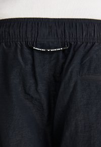 Nærbillede af den sorte Nike Tech shorts talje, med elastik og en lille lynlås lomme på det teksturerede stof.