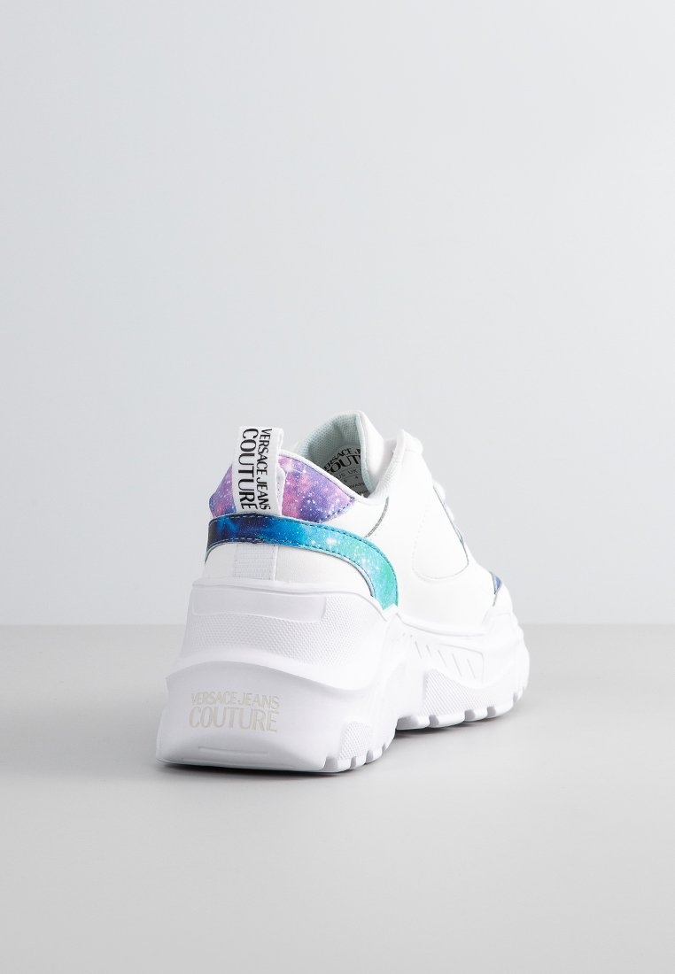 Zapatillas chunky blancas con una suela texturizada, que presentan un acento en el talón iridiscente en azul y púrpura, además de una tira de marca en la parte trasera.