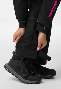 Black waterproof hiking boots, featuring a textured upper, with reflective accents and a sturdy sole, paired with black pants adjusting at the cuff.