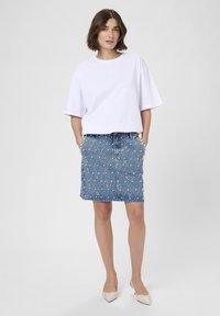 White oversized t-shirt paired with a blue denim skirt featuring floral embellishments and studded accents. Slender cut, knee-length.
