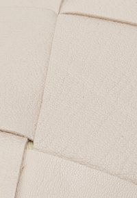 Geweven textuur van wit leer met zichtbare stiksels en subtiele plooien, die het zachte oppervlak benadrukken.