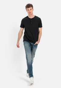 Sort kortærmet henley skjorte med rund halsudskæring og tre knapper, parret med lyseblå slidte jeans og hvide sneakers.