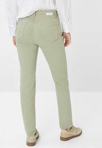 Hellgrüne Slim-Fit-Jeans mit Gesäßtaschen und sichtbaren Nähdetails, kombiniert mit beigen Sneakern. Die Textur wirkt glatt und eng anliegend.