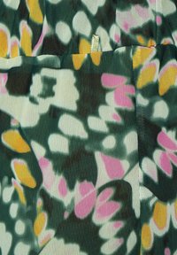 Close-up of floral fabric with green, white, pink, and yellow abstract flower patterns and a small sewn loop detail.