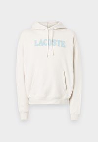 Sweatshirt com capuz creme com bolso canguru, capuz com cordão e textura suave de felpa. Apresenta o logótipo "LACOSTE" bordado felpudo em cores pastel.