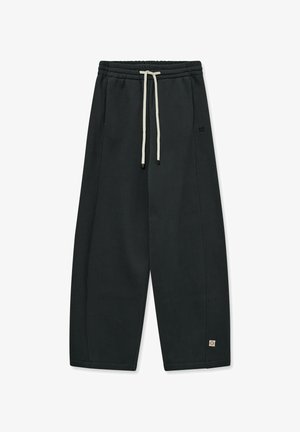 Black sweatpants made of soft material, featuring an elastic waistband with a drawstring and side seams. Includes logo patch on lower side.