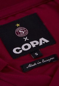 Bordeaux sportshirtlabel met logo's: Servette FC, COPA, en maat 'S'. Labels vermelden materiaaleigenschappen en "Gemaakt in Europa."