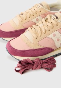 Et par rosa og beige semskede sneakers med tykke beige snører og et ekstra par mørk rosa skolisser ved siden av dem.