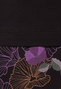 Tela negra con una textura suave que presenta grandes patrones florales en púrpura y naranja. Se puede ver el dobladillo cosido en la parte superior del diseño.